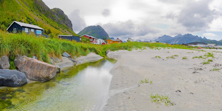 RAMBERG BEACH IN LOFOTEN NORWAY WITH WHITE SAND AND MOUNTAINS - SCENIC COASTAL VILLAGE, SEA, HOUSES, GRASS, ROCKS AND CLOUDY SKY, NORDIC TRAVEL DESTINATION WITH SHORE AND RURAL SETTLEMENT