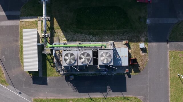 Aerial view of industrial cooling fans and green piping at the Guardian Glass Production Factory with asphalt paths and shadows in Goole, England, United Kingdom.