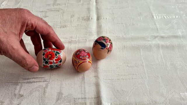 Three hand painted decorative eggs with colorful floral and ornamental designs on a patterned tablecloth, showcasing traditional craftsmanship and festive artistic detail