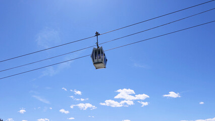 Single Cable Car Gondola Suspended Against a Bright Blue Sky © blueringmedia