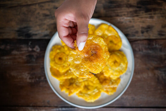 Woman hand picking up delicious patacon from plate on wooden table