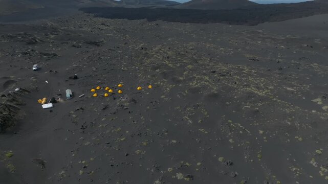 Drone view of Tolbachinsky Dol lava fields and black volcanic sand with a lone off-road vehicle crossing the barren landscape, Kamchatka Krai, Russia