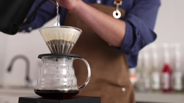 Professional barista preparing drink coffee with drip or filter paper style using the pour over method pouring hot water to brew a caffeine beverage from black bean in cafe restaurant business shop