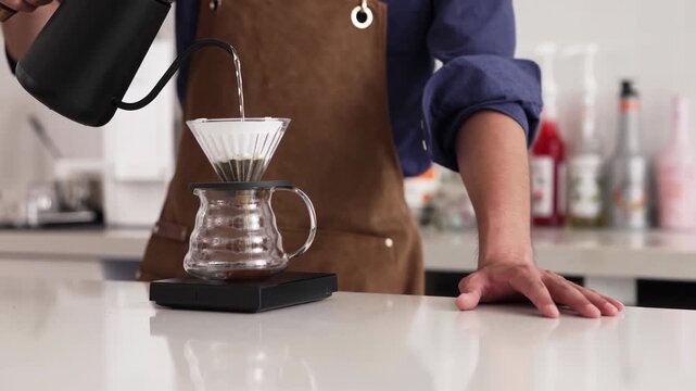 Professional barista pours hot water brew a caffeine beverage from black bean into a cup or mug through paper filter style using the pour over method. coffee maker and drip kettle. Coffee shop concept