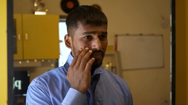 Young Indian male in office college attire adjusts tie while staring into a mirror, unhappy with acne-ridden tanned skin; an intimate bedroom moment reflecting self-image concerns and insecurity