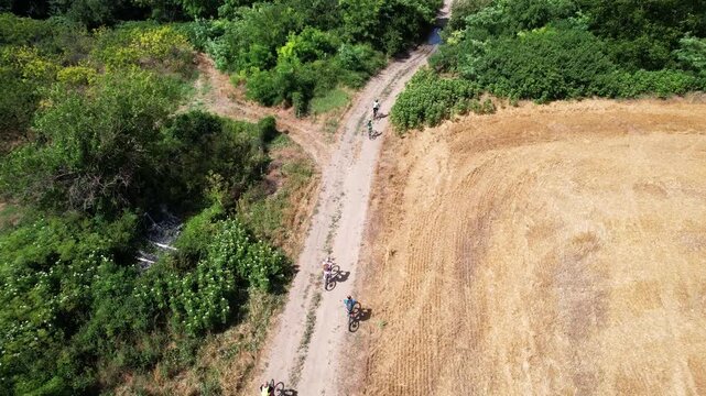 Aerial view of a group of cyclists riding along a dirt path between green and golden agricultural fields in Provadia, Varna, Bulgaria.