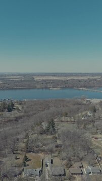 Aerial parallax shot above wooded Hudson Wisconsin bluff neighborhood revealing wide St Croix River, large marina with boat docks and winterized boats with flat farmland beyond
