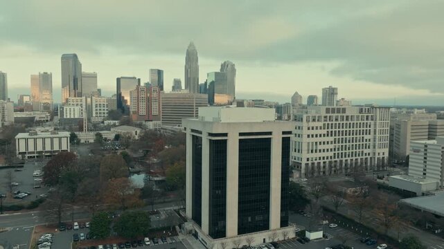 Aerial parallax orbit around the 13-story 301 Midtown office building on South McDowell Street revealing full Charlotte North Carolina skyline under moody overcast sky