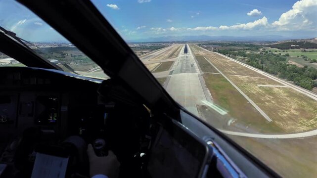 hand of a caucasian copilot at the controls of a jet airplane in a real time final approach and landing at Madrid aiport in a sunny and windy day, with few clouds in a blue sky.