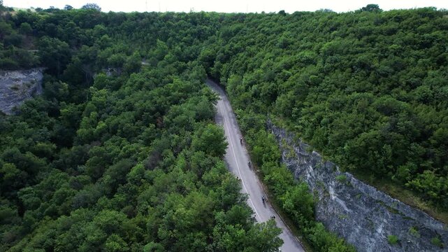 Aerial view of a winding asphalt road with people riding through a dense green forest and rocky cliffs in the canyon near Provadia, Varna, Bulgaria.