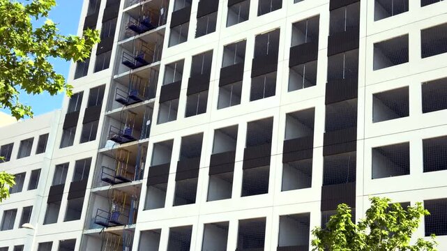 Low angle view of a modern residential building under construction with geometric facade patterns and temporary loading platforms in Madrid, Spain.
