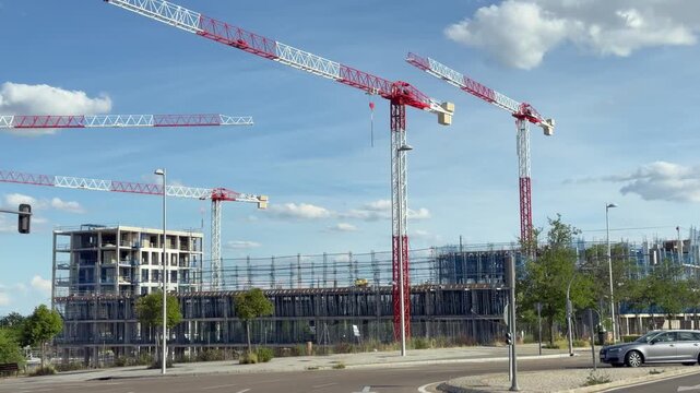 Multiple tower cranes above a large residential construction site with reinforced concrete structures and scaffolding in Madrid, Spain.