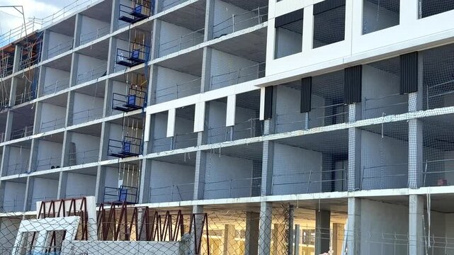 Modern residential apartment facade under construction with temporary construction hoists and exposed structural levels in Madrid, Spain.