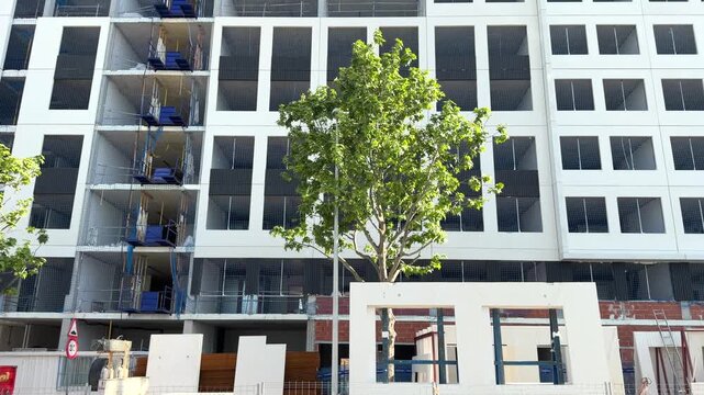 Modern residential building facade under construction with temporary construction hoists and safety netting in Madrid, Spain.