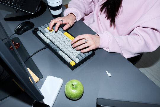 Young adult woman typing on mechanical keyboard at desk, working on computer in home office. Suitable for remote work, productivity, freelance job, digital workflow marketing