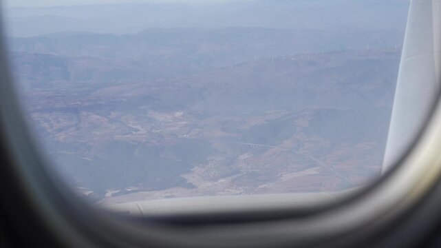 view through airplane window while flying over mountain range over Kunming area in China over cloud and mountain submit in daytime,high plains of china near Tibet area from airplane