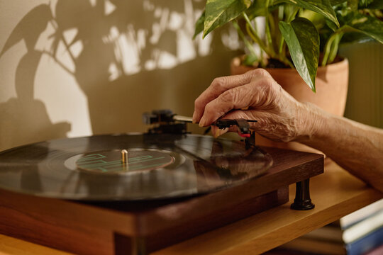 Close up of senior hand placing needle on vinyl record player, playing music at home and evoking nostalgia. Suitable for retirement lifestyle, memory care, leisure, wellness campaigns