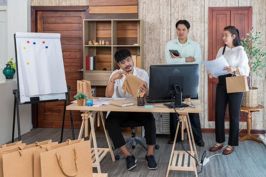 Startup team reviewing paper bag samples for their product packaging:Colleagues inspecting the quality and design of packaging from a supplier.Focus on branding,cost analysis and e-commerce logistics.