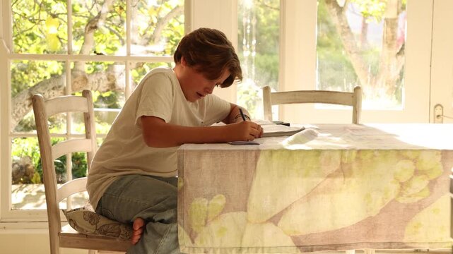 12 year old boy doing homework at kitchen table at sunset