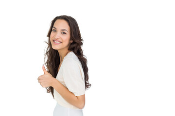Fototapeta premium Adult woman smiling and giving thumbs-up while posing in white studio wearing beige top, copy space