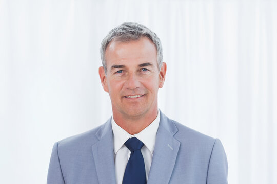 Middle-aged man posing for corporate headshot in studio wearing light gray suit and navy tie