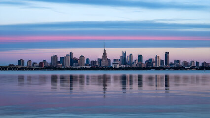 Naklejka premium City skyline reflects on calm water at sunset over landscape