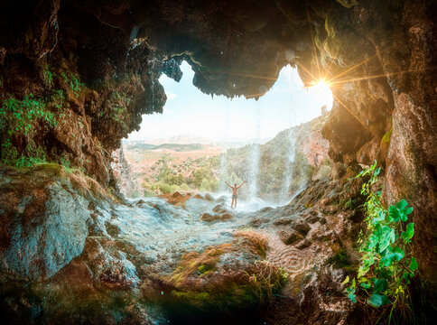 Cave with a waterfall and the silhouette of a man opening his arms