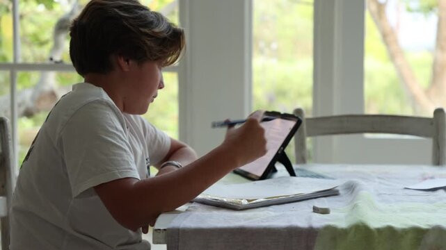 12 year old boy doing homework at kitchen table  using a tablet computer