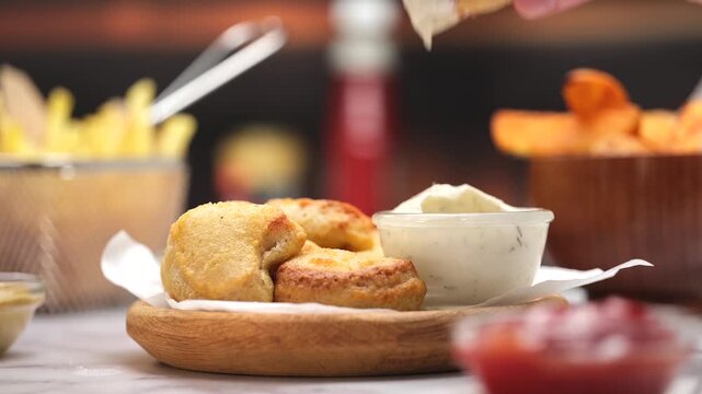 Chicken nuggets dipped in creamy sauce by hand in warm kitchen setting