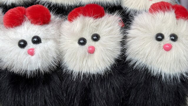 Cute fluffy pompom creatures with black eyes and pink noses line up closely in a row