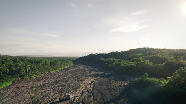 Wide aerial view of a rugged 4x4 driving along the dry riverbed of Sukhaya Rechka on the route to Avachinsky Volcano, Kamchatka Krai, Russia at sunset