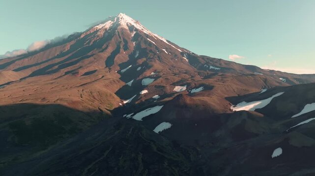Aerial footage of Koryaksky Volcano with snowfields on rugged volcanic slopes at golden hour, in Kamchatka Krai, Russia, clear sky and dramatic mountain scenery