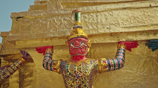 Colorful guardian demon figure supporting golden chedi at Wat Phra Kaew in Bangkok, traditional Thai temple art in Thailand