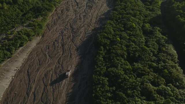 Drone view of a truck driving along the dry riverbed of Sukhaya River on the road toward Avachinsky Volcano, Kamchatka Krai, Russia in summer light