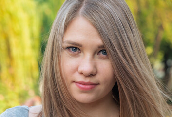Naklejka premium Headshot of a young woman with straight light blonde hair and blue eyes outdoors in natural light