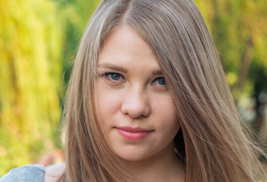 Headshot of a young woman with straight light blonde hair and blue eyes outdoors in natural light