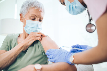 Syringe, injection and nurse with senior woman in clinic for vaccine, virus safety or medical treatment. Needle, gloves and healthcare worker with elderly patient for vitamin shot at consultation. © peopleimages.com