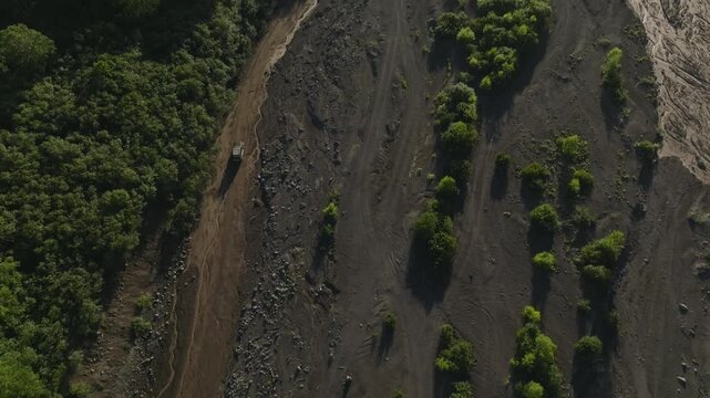Drone footage over the Sukhaya River dry channel and a dirt road leading toward Avachinsky Volcano, Kamchatka Krai, Russia, with green forest and volcanic ash slopes