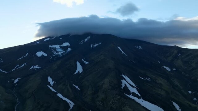 Drone footage of Avachinsky Volcano with dark volcanic slopes and scattered snowfields under a clear sky, Kamchatka Krai, Russia, remote wilderness landscape