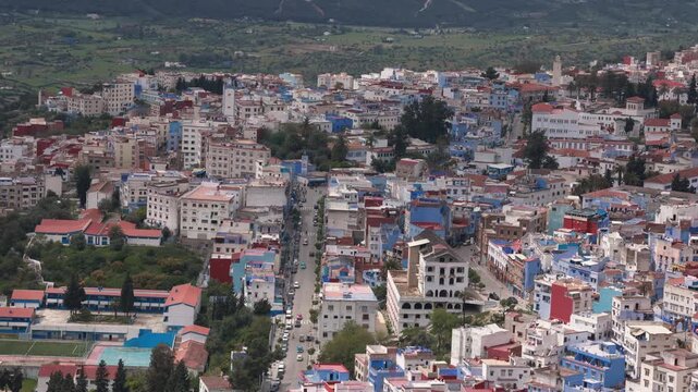 Panoramic view of Chefchaouen with its blue buildings, bustling streets, and lush green mountains in Morocco