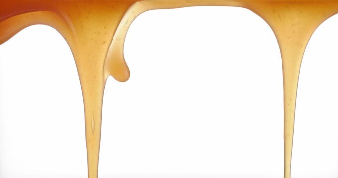 Close up macro of fresh homemade caramel sauce flowing and stretching on a white background. Smooth, glossy and sweet texture of soft caramel in motion. Dessert topping concept with rich golden color