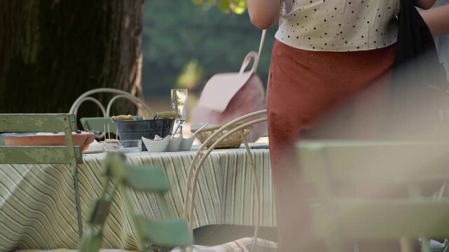 People walking past a dining table during a corporate lunch event in a Limoges natural area. Festive table settings ready for employees. Static shot.