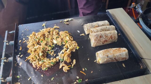 Street vendor preparing traditional Kottu Roti on a hot metal griddle in Ella, Sri Lanka, chopping flatbread with vegetables and spices in a lively display of local street food culture