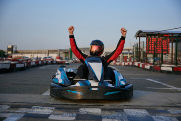 Naklejka premium A go-kart racer celebrates a successful lap, raising hands in triumph on the track