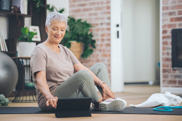 Obraz premium Senior, woman and exercise with tablet for tutorial, workout guide or online tips on floor in home. Elderly, female person or training schedule with technology on mat for pilates or fitness app