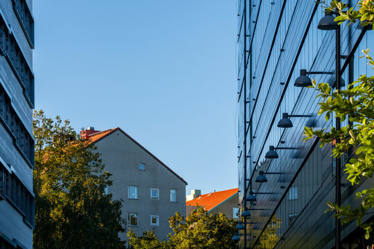 Looking down a Stockholm street where modern glass facade meets historic architecture with trees and sky framing a bold perspective and contrast