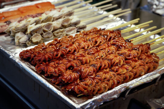 Close-up of fresh seafood skewers including abalone and octopus at a busy night market in Seoul, South Korea.