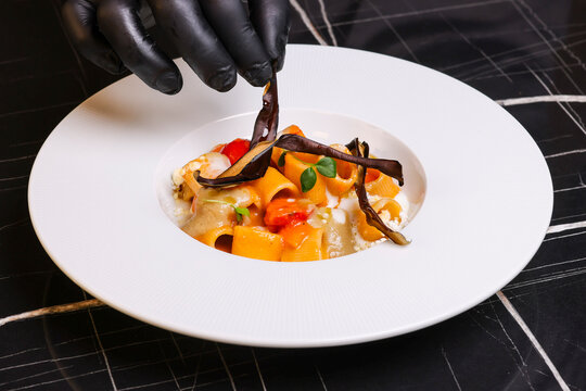 Piatto di pasta con crema di melanzane, pomodorini freschi e melanzane fritte servito in un ristorante elegante