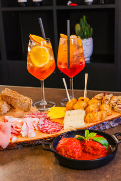 Aperitivo servito in un bar con spritz, tagliere di salmi e formaggi, polpette al sugo e pane caldo