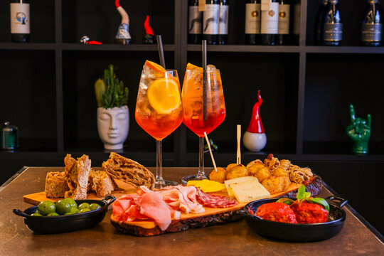Aperitivo servito in un bar con spritz, tagliere di salmi e formaggi, polpette al sugo e pane caldo